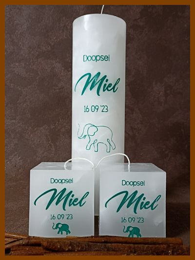 een hoge witte vierkante kaars voor Miel met een olifantje. De kleine kaarsjes zijn voor peter en meter ook met de naam Miel en geboortedatum.